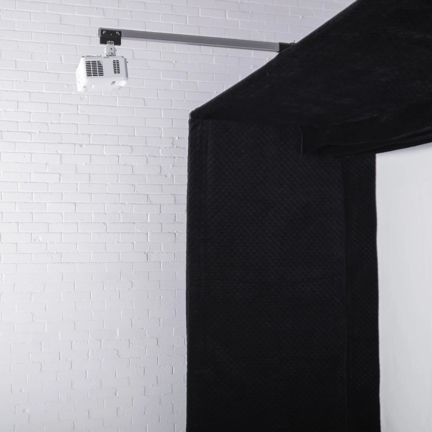 Black quilted golf simulator enclosure with mounted projector against white brick wall