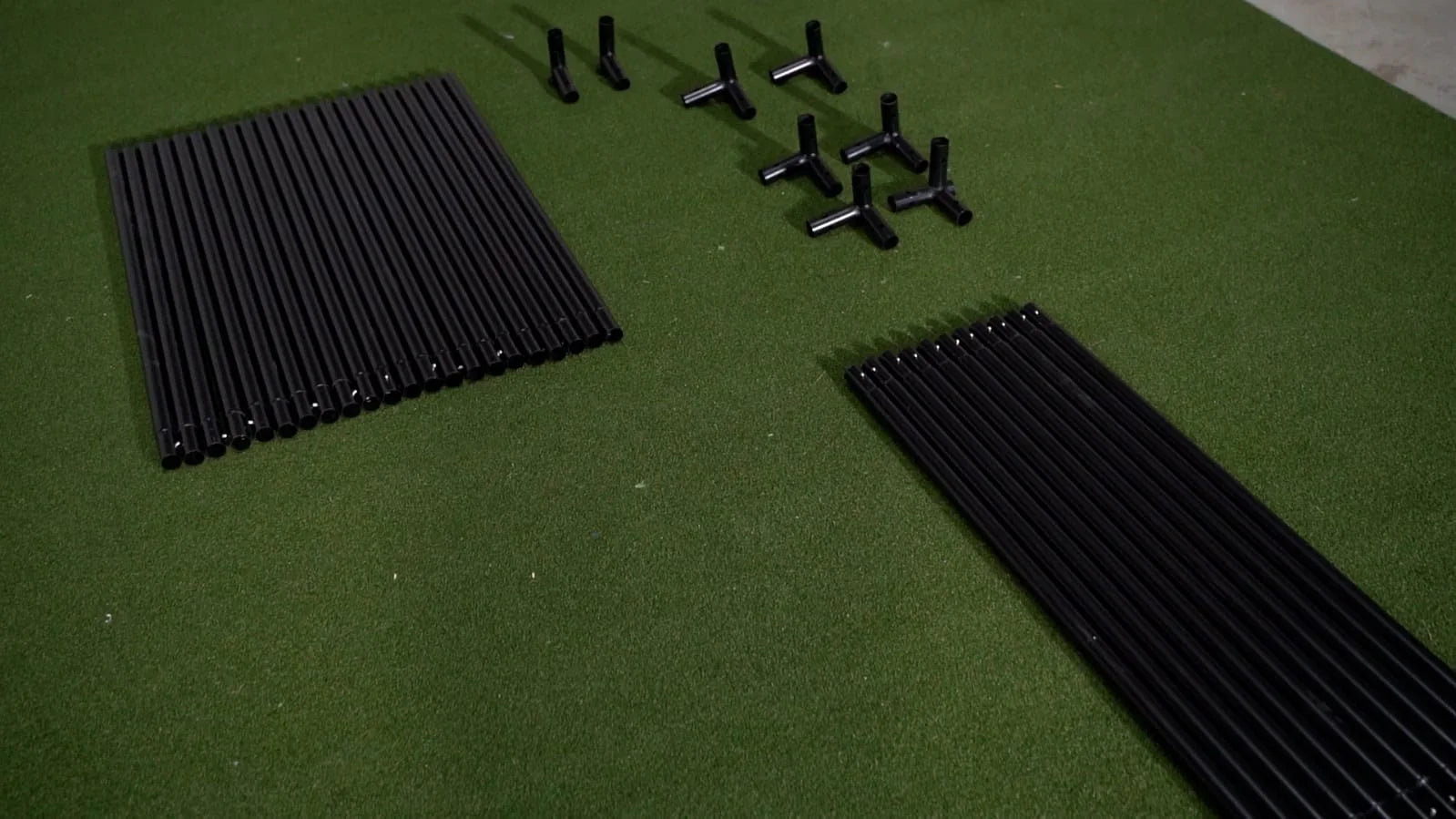 Black golf simulator enclosure poles and connectors on green turf mat for indoor golf setup