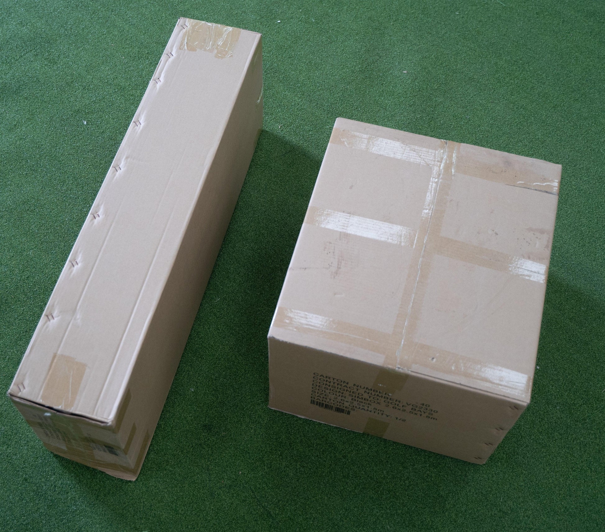 Two packaged golf simulator enclosures on green turf, ready for indoor golf setup