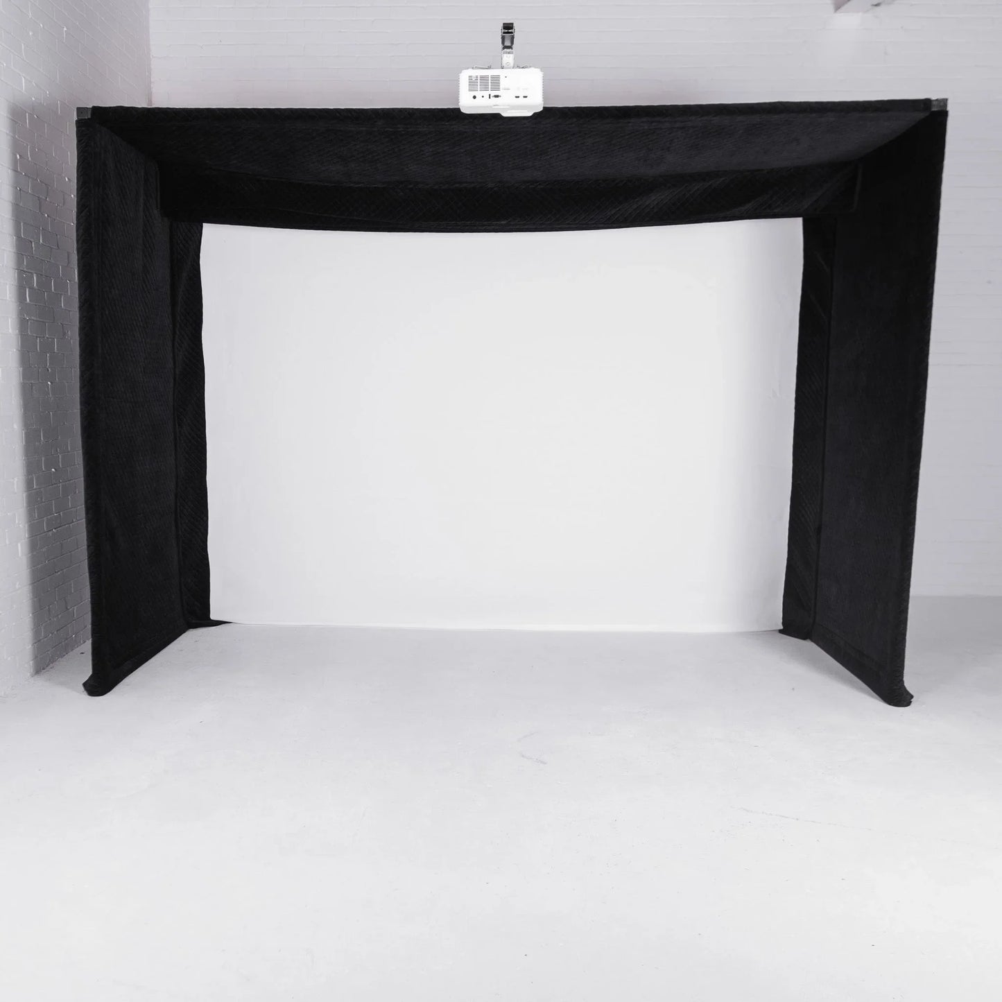 Black golf simulator enclosure with projector mounted above white impact screen for indoor practice