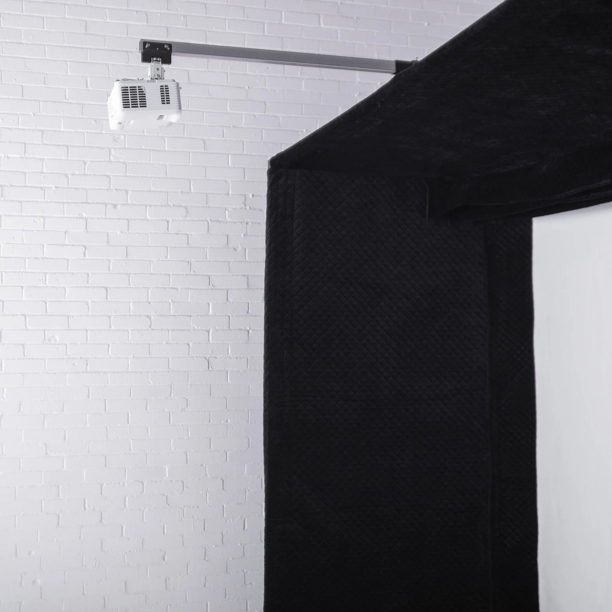 Black quilted golf simulator enclosure with mounted projector against white brick wall