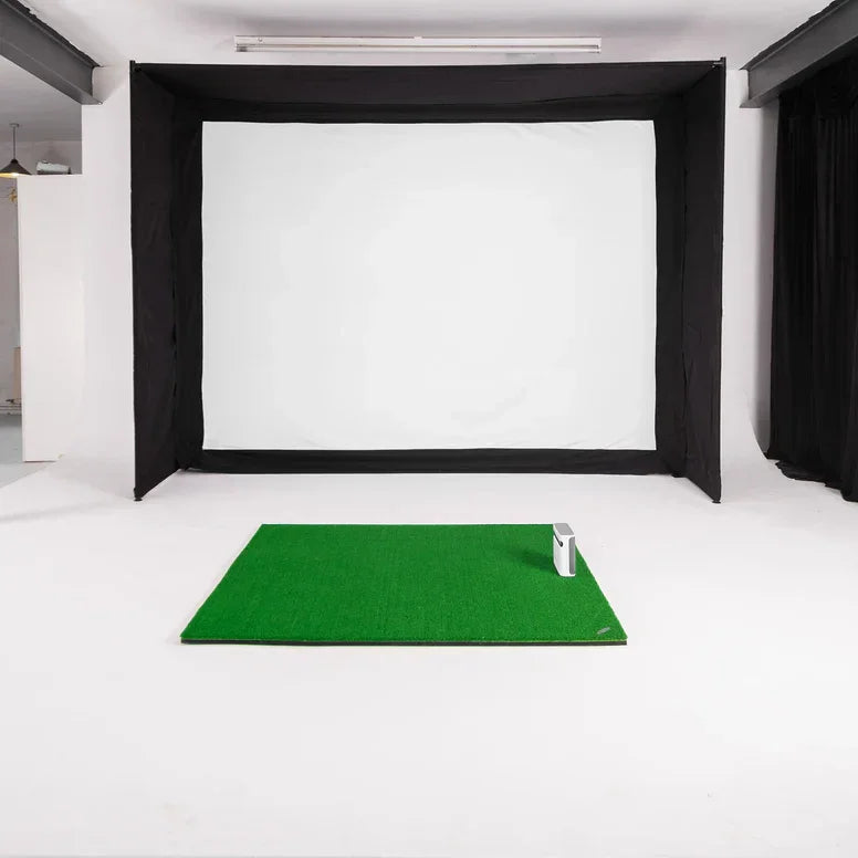 Indoor golf simulator setup with green mat, impact screen, and enclosure for home practice