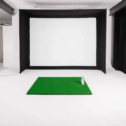 Indoor golf simulator setup with green mat, impact screen, and enclosure for home practice