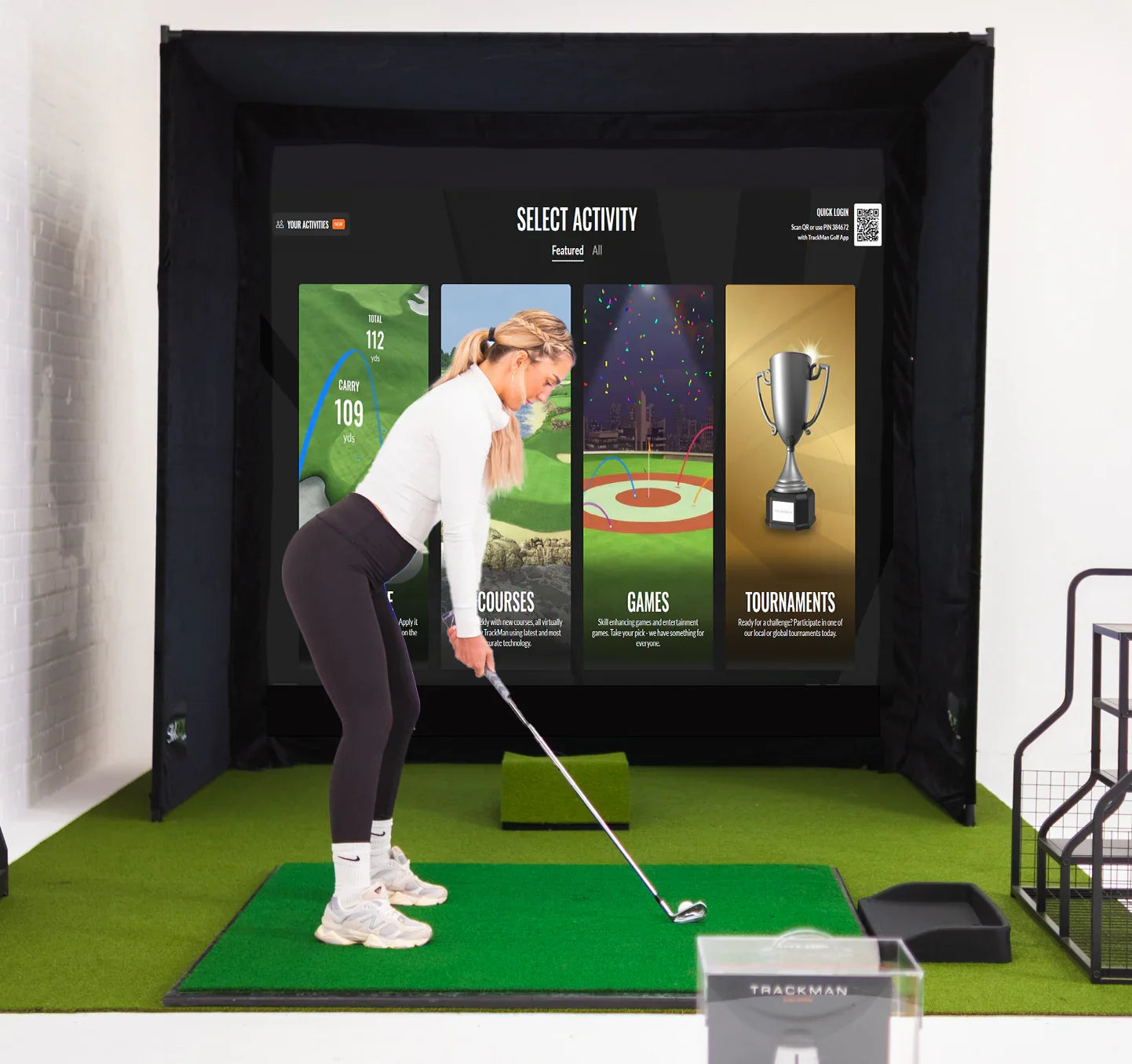 Woman practicing golf swing on indoor simulator with TrackMan, impact screen, and turf mat for home or commercial use