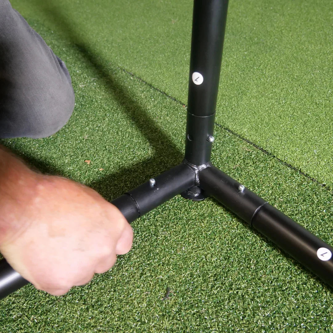 Hand assembling black golf simulator frame on green turf mat