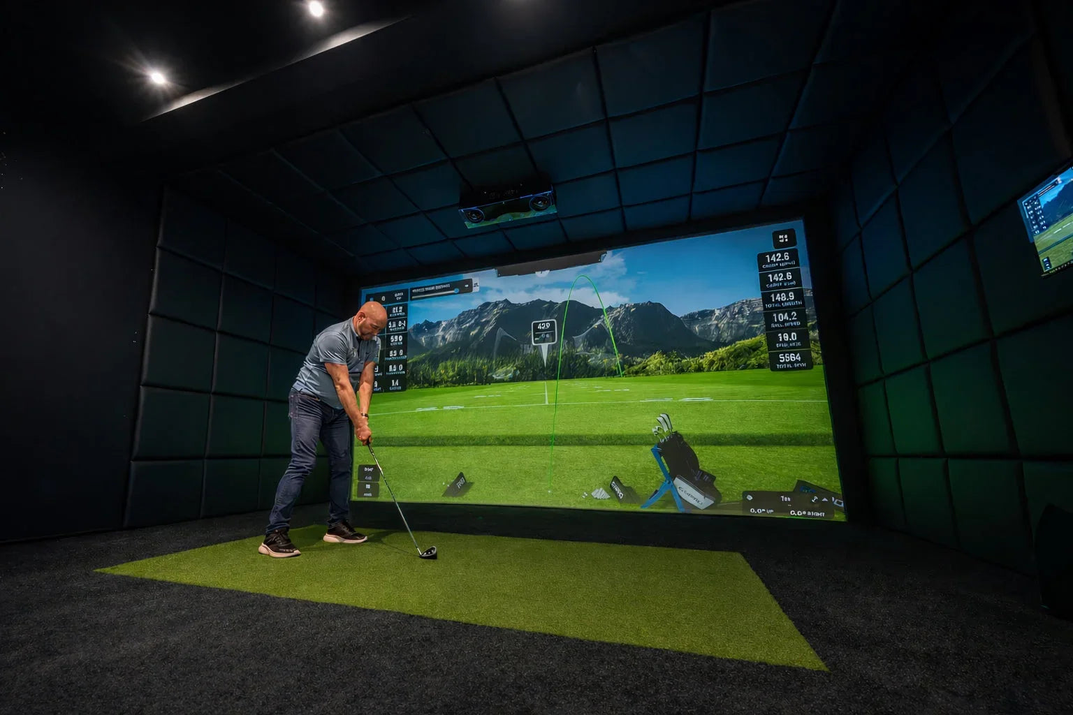 Man practicing golf indoors with simulator, impact screen, and mat in a soundproofed room